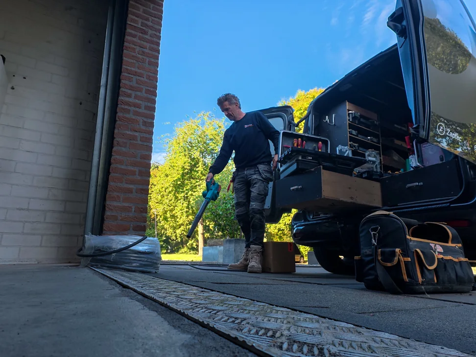 Monteur ruimt de werkplek bij de garage op