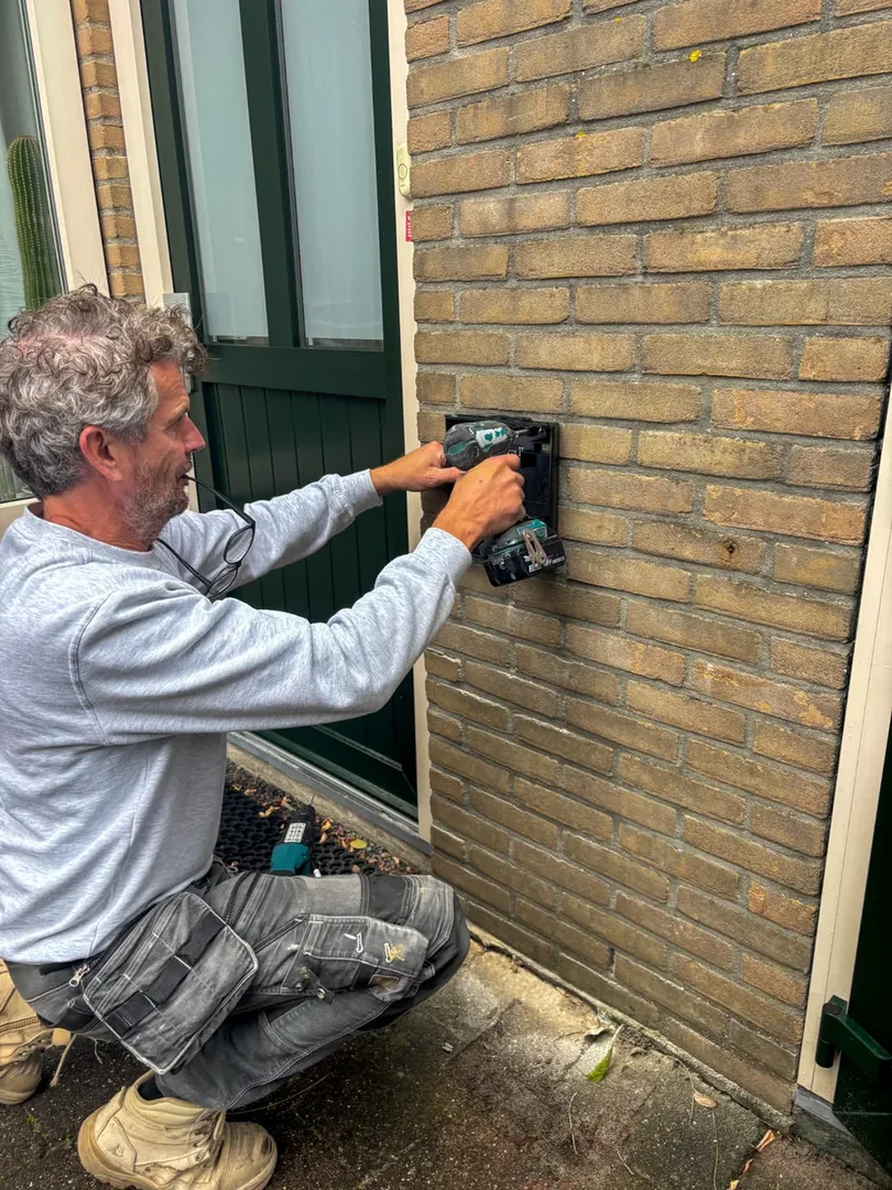 Monteur bevestigt de montageplaat van de laadpaal aan de bakstenen gevel in Maarssen