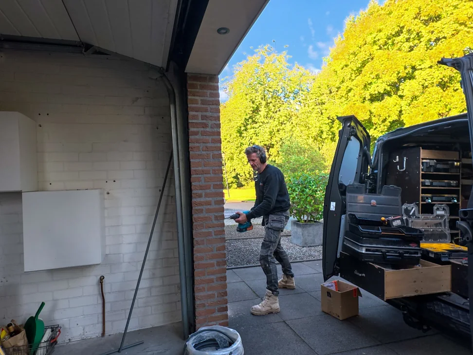 Monteur boort bij de garagemuur voor de laadpaalinstallatie
