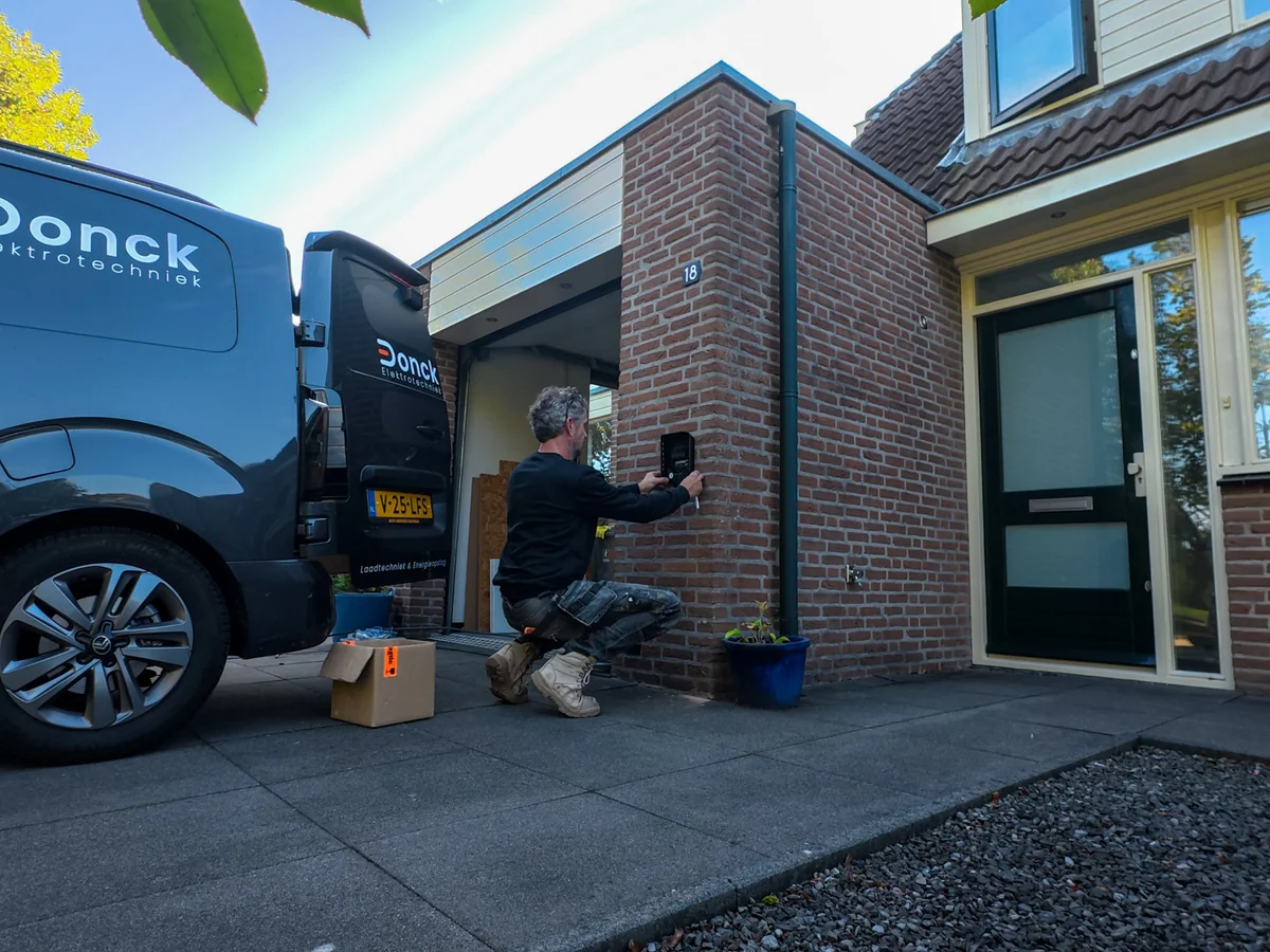 Monteur bevestigt een zwarte kast aan de bakstenen gevel bij de woning