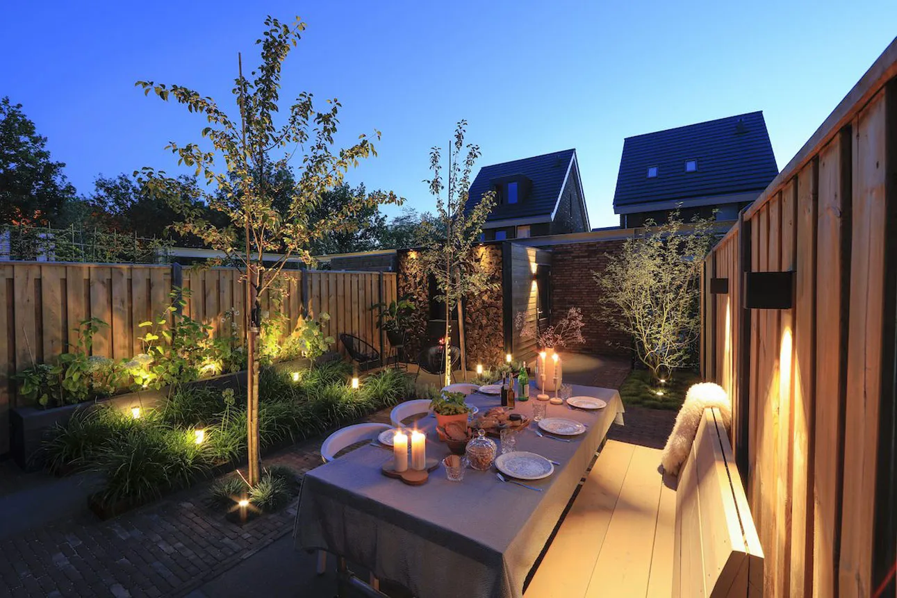 Sfeervol verlichte tuin met terras- en gevelverlichting in de avond